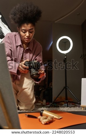 Black female photographer taking photo of ginger and cosmetic cream on digital camera at home studio. Creating beauty and body care content for photostocks, commerce, social networks and advertising