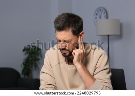 Man suffering from ear pain on in room Royalty-Free Stock Photo #2248029795
