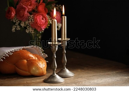 Challah bread covered with a special napkin and two burning candles  on the wooden table. Traditional Jewish Shabbat ritual. Shabbat Shalom.