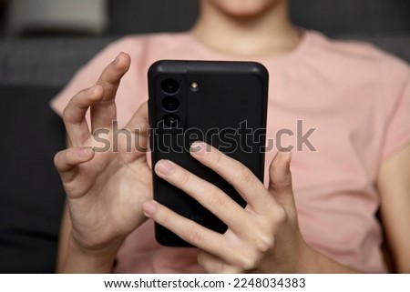 A teenage girl using a smartphone, presses her finger, reads social networks on the Internet, types text or plays video games, a mobile phone in two hands close-up