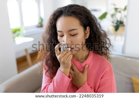 Asian woman using inhaler while suffering from asthma at home. Young woman using asthma inhaler. Close-up of a young Asian woman using asthma inhaler at home. Royalty-Free Stock Photo #2248035319