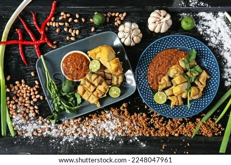 Flat lay photo of Batagor (fish cake), Indonesia's signature street food served with peanut sauce, plating in a black wooden table