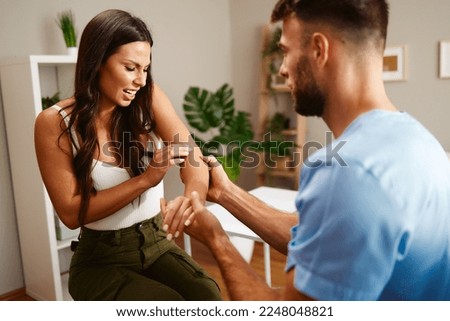 Young woman with elbow pain is being examined by doctor Royalty-Free Stock Photo #2248048821