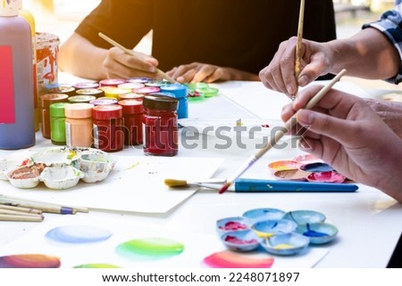 Learning to use poster color to draw various pictures of asian boys on a table outside classroom with his female art teacher, raising teen and adult helps kids school project concept.