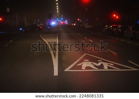 Wet asphalt, reflection of neon lights. Big city in the fog at night. With traffic signs - attention children, school.