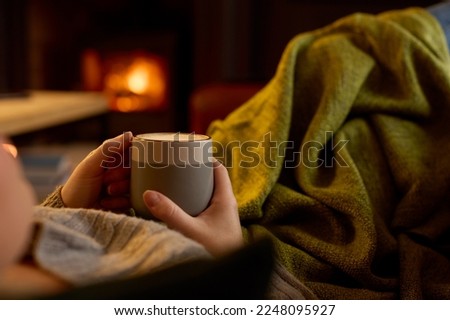 Close Up Of Woman At Home In Lounge Lying On Sofa With Cosy Fire With Hot Drink
