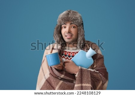Young man with cup and hot water bottle on color background