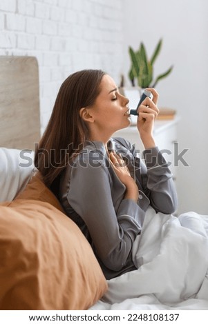 Sick young woman with inhaler in bed Royalty-Free Stock Photo #2248108137