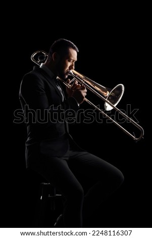 Man playing a trumpet and sitting on a chair isolated on black background Royalty-Free Stock Photo #2248116307