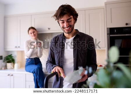 Couple At Home In Kitchen With Man Doing Washing Up Royalty-Free Stock Photo #2248117171