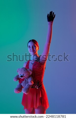 Wow, success, win. Wow, success, win. Happy young girl, female figure skater in stage costume standing with raising hand isolated over green-blue background in neon. Sport, winner emotions