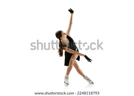 Studio shot of beautiful female figure skater in black festive stage dress practicing base elements of short program. Concept of winter sports, flexibility, beauty and ad