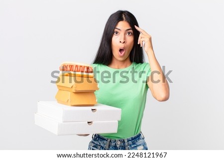 pretty hispanic woman looking surprised, realizing a new thought, idea or concept and holding take away fast food boxes