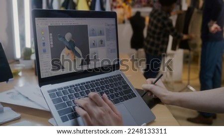 Female fashion designer develops future design of clothes in 3D modeling program on laptop using digital tablet and stylus. She works in atelier workshop. Fashion and technologies in business concept. Royalty-Free Stock Photo #2248133311