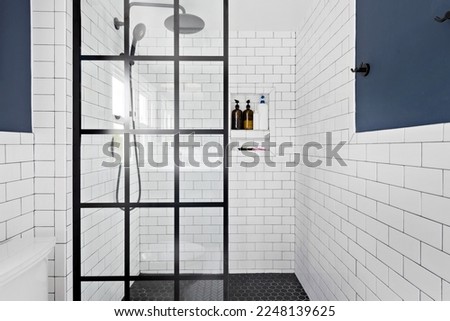 Styled Updated Bathroom Interior. Renovated white bathroom with contemporary design and modern fixtures. Glass enclosed shower with white subway tile and rainfall showerhead. Royalty-Free Stock Photo #2248139625