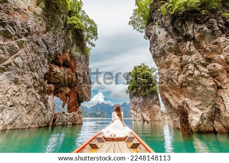 Back View of Young Female Tourist in Dress and Hat at Longtail Boat near Famous Three rocks with Limestone Cliffs at Cheow Lan Lake. Travel Woman Sitting on Boat in Khao Sok National Park in Thailand Royalty-Free Stock Photo #2248148113