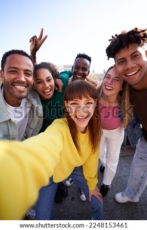 Multiethnic group of friends taking a selfie outdoors. Young people addicted to technology using mobile app to take photos looking at camera. Copy space. Vertical.
