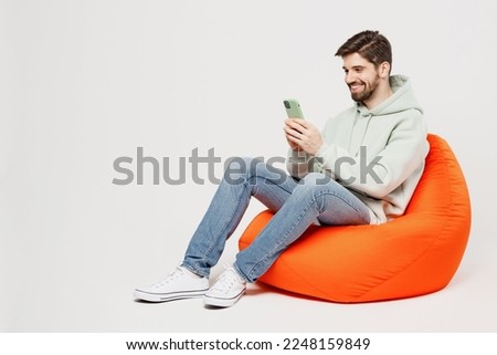 Full body young satisfied happy fun cheerful man wear mint hoody sit in bag chair hold in hand use mobile cell phone isolated on plain solid white background studio portrait. People lifestyle concept Royalty-Free Stock Photo #2248159849