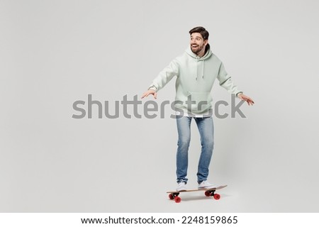 Full body side profile view fun young excited amazed happy smilign caucasian man wearing mint hoody riding skateboard isolated on plain solid white background studio portrait. People lifestyle concept
