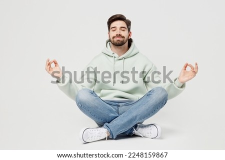Full body spiritual tranquil young man wear mint hoody hold spreading hands in yoga om aum gesture relax meditate try to calm down isolated on plain solid white background. People lifestyle concept
