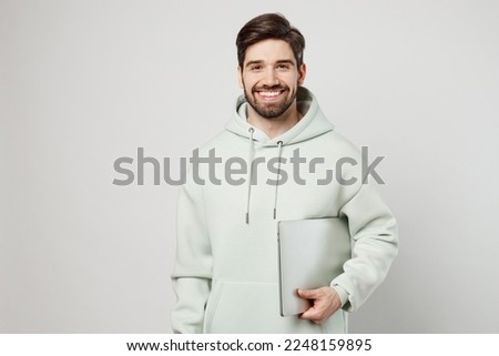 Young smiling programmer happy fun caucasian man wearing mint hoody hold use work on laptop pc computer look camera isolated on plain solid white background studio portrait. People lifestyle concept Royalty-Free Stock Photo #2248159895
