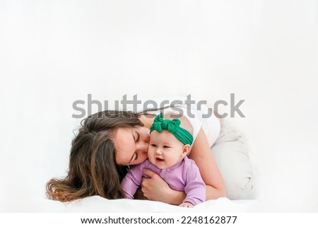 A young mother and baby girl are sitting on the floor on a white background. Festive bright clothes