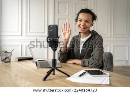 At work in the office, a freelancer online video communicates smiling with people via video link, uses a phone on a tripod.