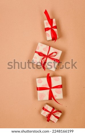 Gifts boxes in wrapping paper tied red ribbon, paper hearts on beige background. Concept of the St. Valentine's day, weddings, engagements, Mother's Day, birthday. Greeting card with place for text 