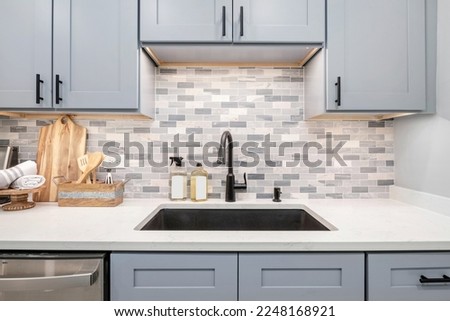 Style Home Still Lifestyle Image. Contemporary Kitchen Design with Powder Blue Cabinets and Matte Black Finish. Gray and White Tile Backsplash. Styled Kitchen Counters. Social Media Banner.