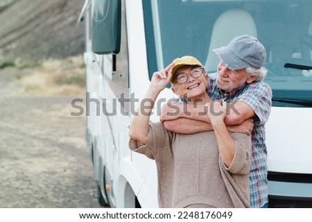 Beautiful senior couple on a leisure trip standing outside a camper van tenderly embracing. Handsome retired caucasian couple enjoying freedom and alternative life in camper van
