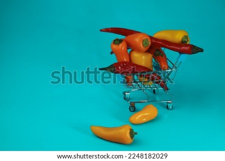 in a shopping cart with shopping wheels lie orange and yellow bell peppers on a bright turquoise background. for banners screensavers stickers flyers business cards