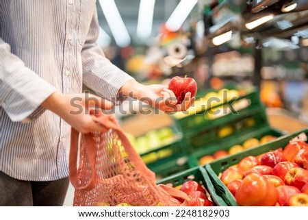 Unrecognizable woman putting an apple in a reusable shopping bag. Woman hands holding an apple and a eco friendly bag at supermarket.