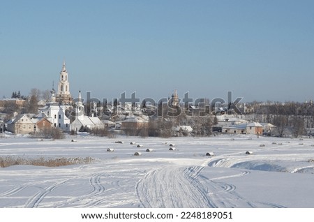 snow-covered field with twisted haystacks, houses and russian orthodox churches of suzdal in the background