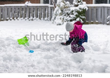 Little child playing with snow and showel outdoors near house in winter. Wintertime fun outdoor activities for children. Royalty-Free Stock Photo #2248198813