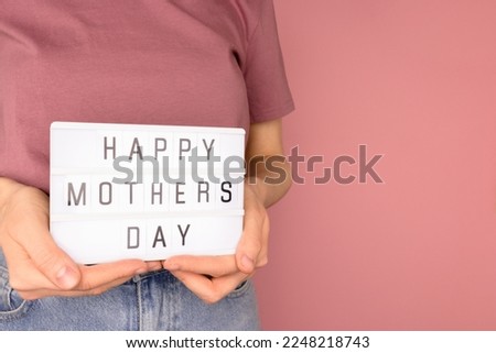 Happy Mothers Day. Woman hold in hands lightbox with letters in front of pink background. 