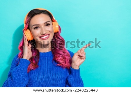Photo of shiny optimistic girl dressed blue sweater touch headphones directing empty space isolated on vibrant teal color background