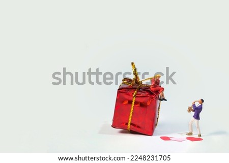 a saxophonist plays his girlfriend sitting on a red gift package a love song for valentines day. White background Royalty-Free Stock Photo #2248231705