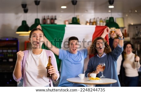 Company of screaming young adult sports fans waving flag of Italy and supporting national team with beer in bar