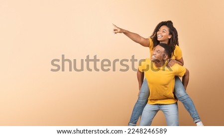 Excited african american couple having fun, lady piggybacking guy and pointing finger at copy space on yellow background, demonstrating place for advert, panorama Royalty-Free Stock Photo #2248246589