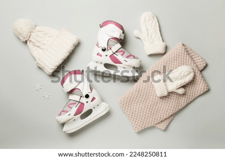 Ice skates and knitted hat on color background, top view