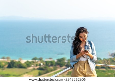 Young Asian woman tourist using mobile phone booking hotel or online shopping during travel at tropical island in summer sunny day. Attractive girl enjoy outdoor lifestyle in beach holiday vacation.