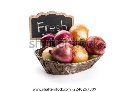 Red and yellow cooking onions in a basket on a market table with a FRESH sign isolated on white