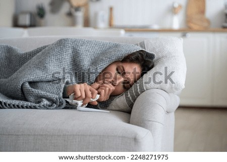 Sick exhausted woman lying on couch wrapped in blanket and coughs after being infected with dangerous flu or viral infection. Suffering unhappy girl with handkerchief and thermometer needs help doctor Royalty-Free Stock Photo #2248271975
