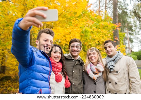 season, people, technology and friendship concept - group of smiling friends with smartphone taking selfie in autumn park