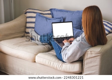 Mockup image of a woman working and typing on laptop computer with blank screen on sofa at home