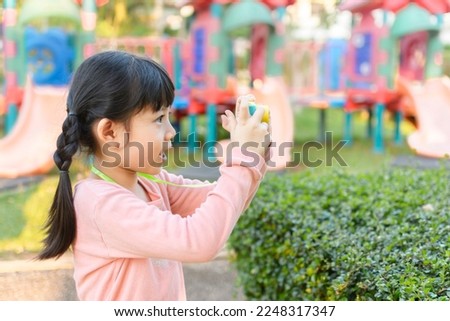 Cute Little Asian Thai Girl taking pictures with toy camera, in Playground.