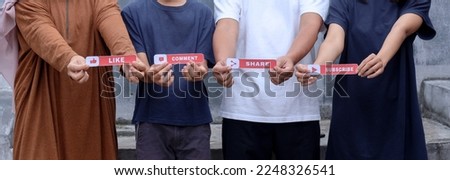 Cropped image of four young people showing printed paper with Like, Comment, Share, and Subscribe text. Vlogger concept.