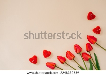 Bouquet of tulips and red heart candles on a beige background with copying space. Festive greeting card for Valentine's Day