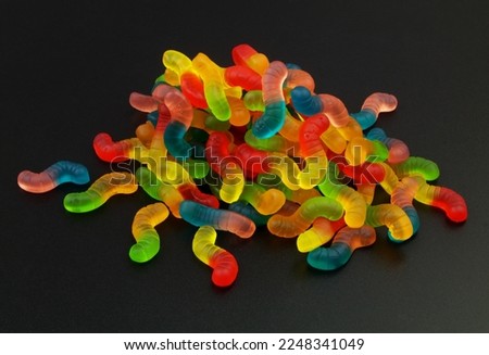 Big heap of vivid multicolored gummy worms on black.