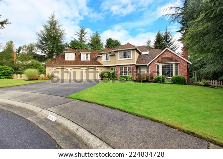 Luxury house exterior with brick trim, tile roof and french windows. House with three car garage and asphalt driveway
